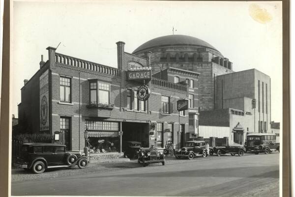 Historische zwart-witfoto van Garage Fissette aan het begin van de Scharnerweg in Maastricht. Voor het bakstenen garagepand staan verschillende personenauto&rsquo;s uit het interbellum geparkeerd. Aan de gevel hangen grote reclameborden voor onder meer Garage, Texaco en Buick.